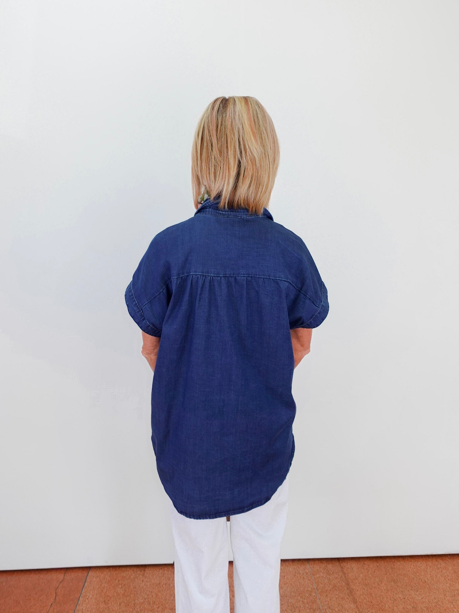 Person wearing a blue shirt standing against a white wall