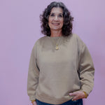 Woman wearing a beige sweater and blue jeans against a purple background