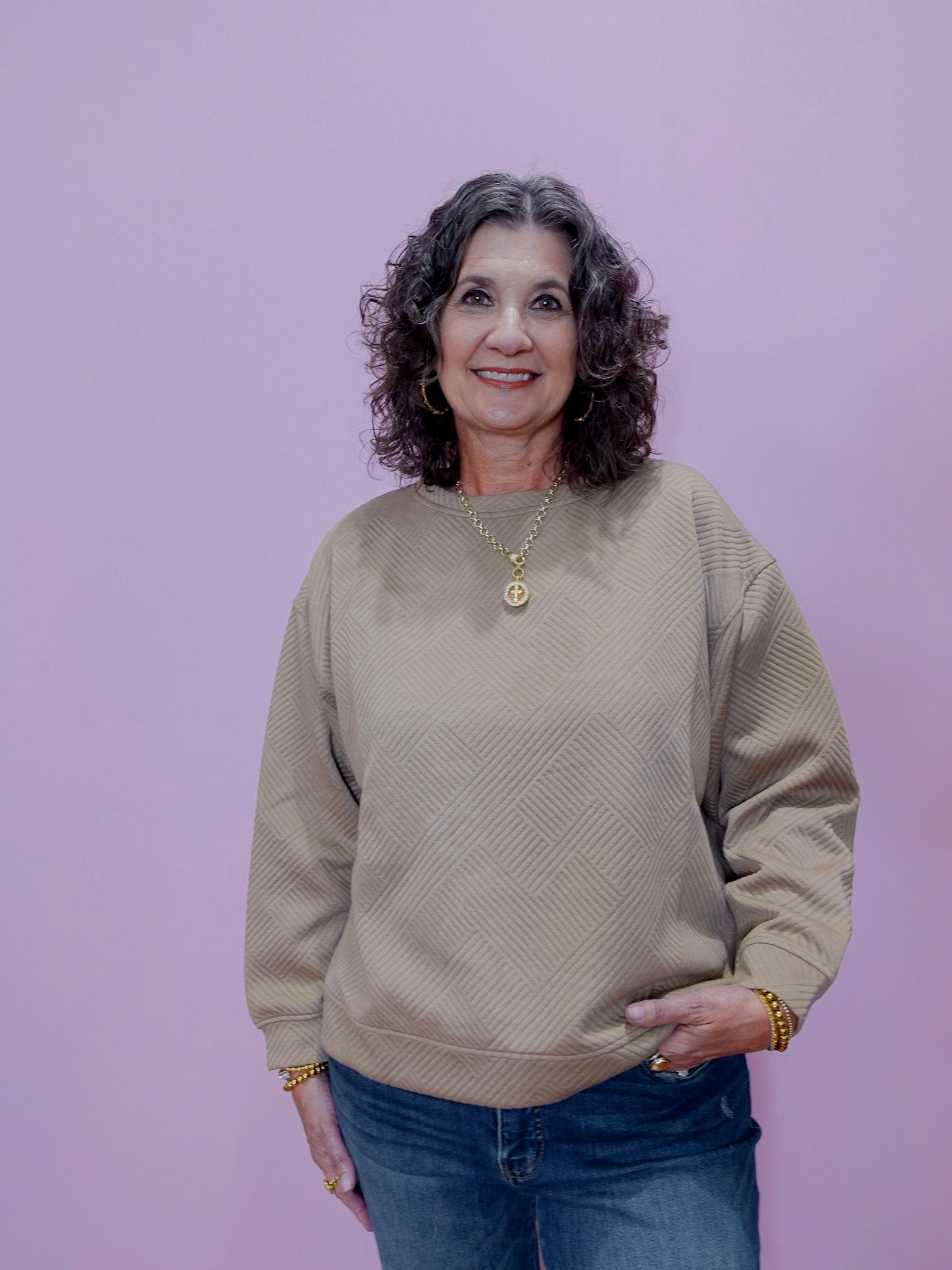 Woman wearing a beige sweater and blue jeans against a purple background