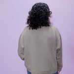 Person wearing a beige sweater with a textured pattern on a light purple background