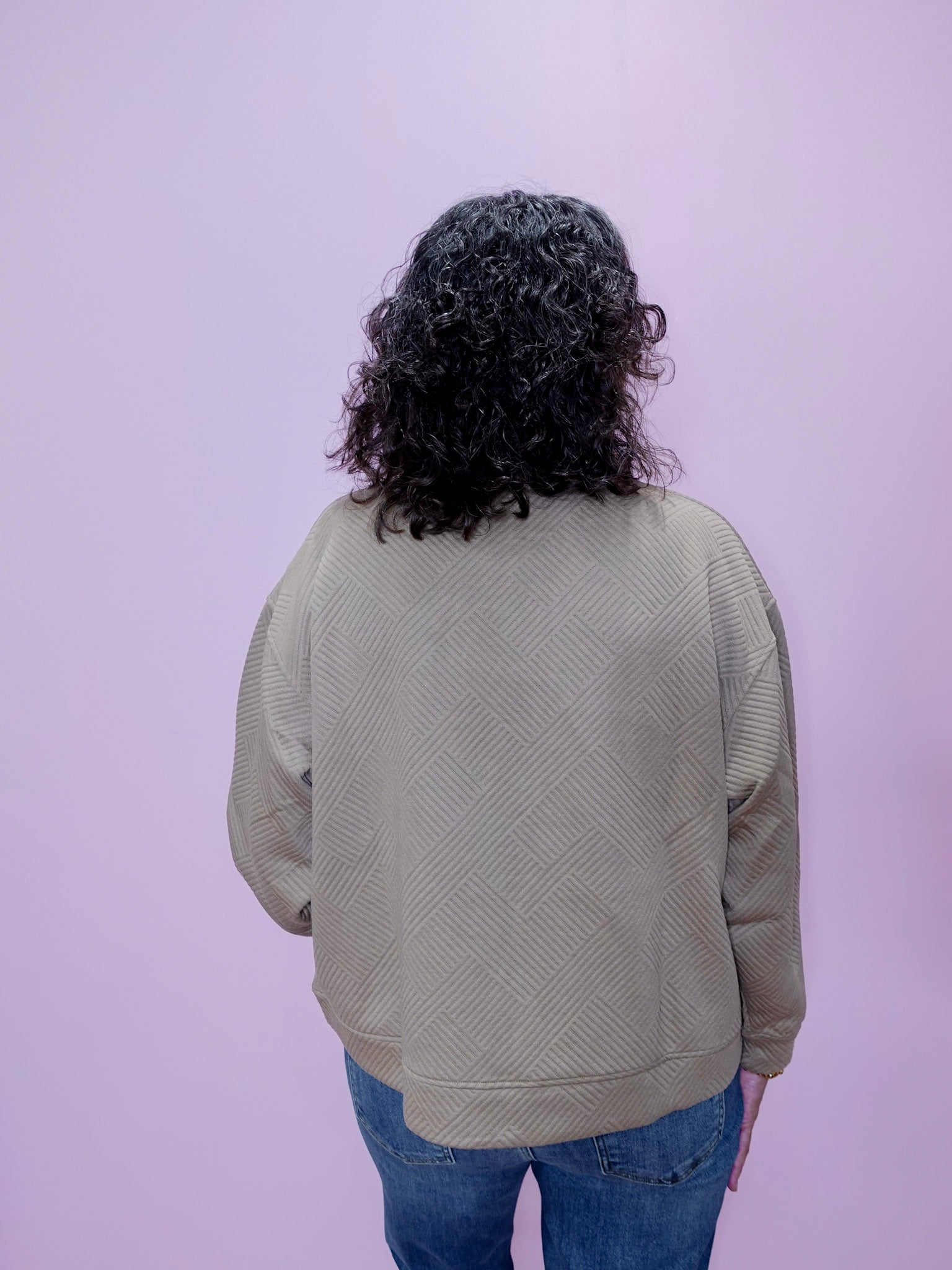 Person wearing a beige sweater with a textured pattern on a light purple background