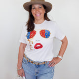 Woman wearing a white t-shirt with colorful sunglasses and lips design, denim shorts, and a straw hat.