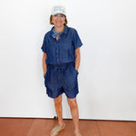 Person wearing a blue romper and white cap against a white wall.