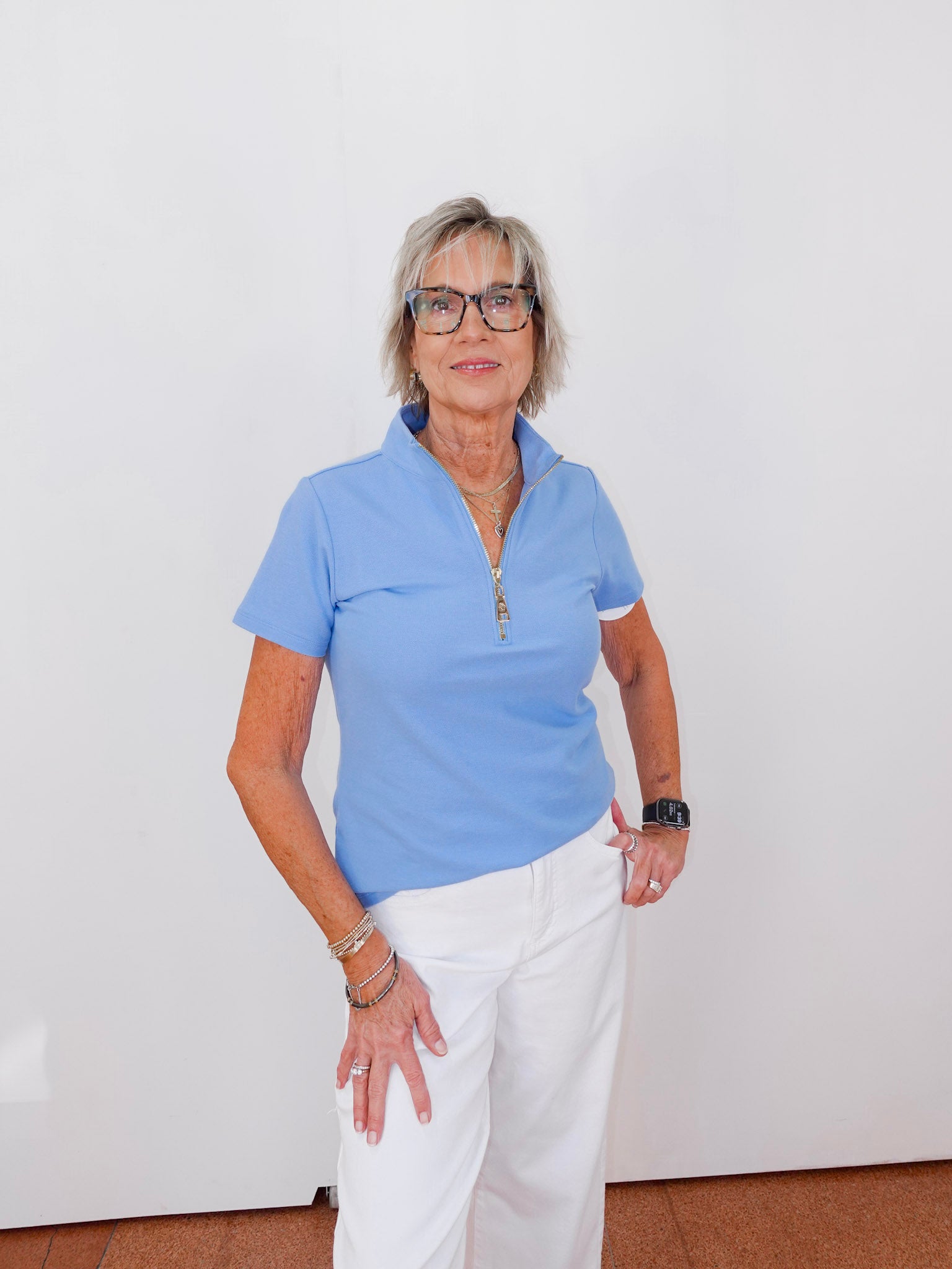 Woman wearing a light blue polo shirt and white pants against a plain background
