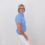 Woman wearing a blue shirt and white pants against a white wall
