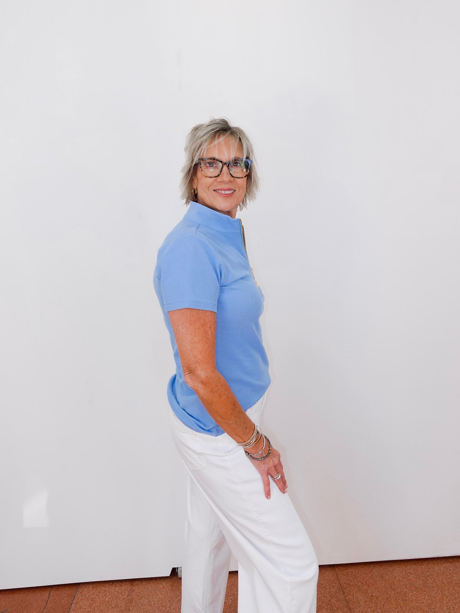 Woman wearing a blue shirt and white pants against a white wall