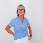 Woman wearing a blue polo shirt and white pants against a plain background