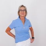 Woman wearing a blue polo shirt and white pants against a plain background