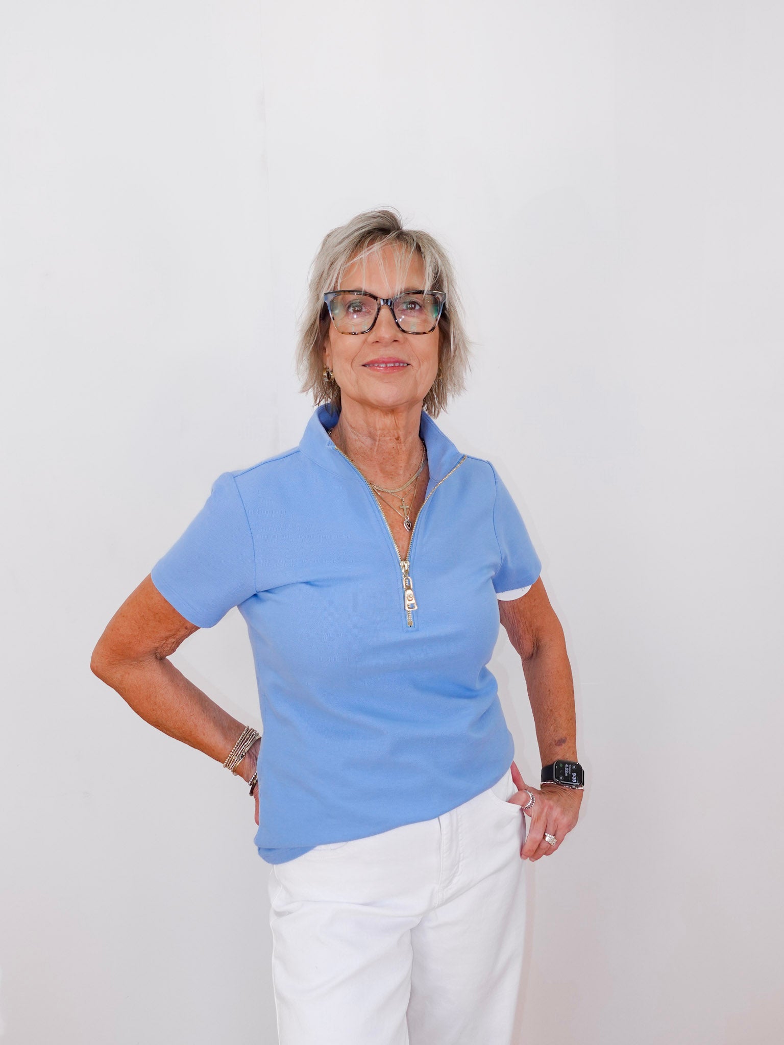 Woman wearing a blue polo shirt and white pants against a plain background