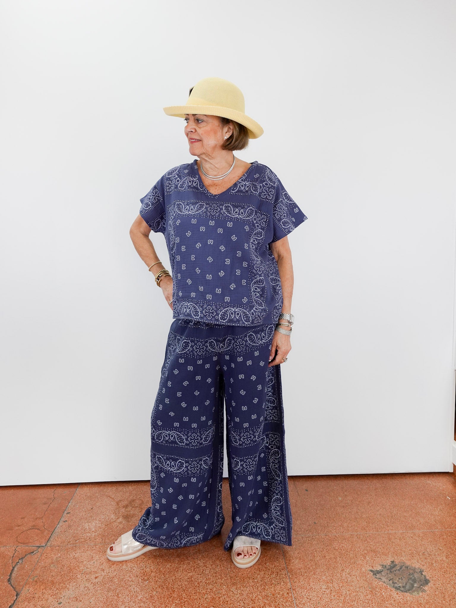 Person wearing a blue bandana print outfit with a hat against a white wall.