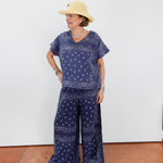 Person wearing a blue bandana print outfit with a hat against a white wall.