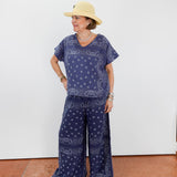 Person wearing a blue bandana print outfit with a hat against a white wall.