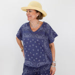 Woman wearing a blue paisley outfit with a beige hat on a white background