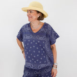 Woman wearing a blue paisley outfit with a beige hat on a white background