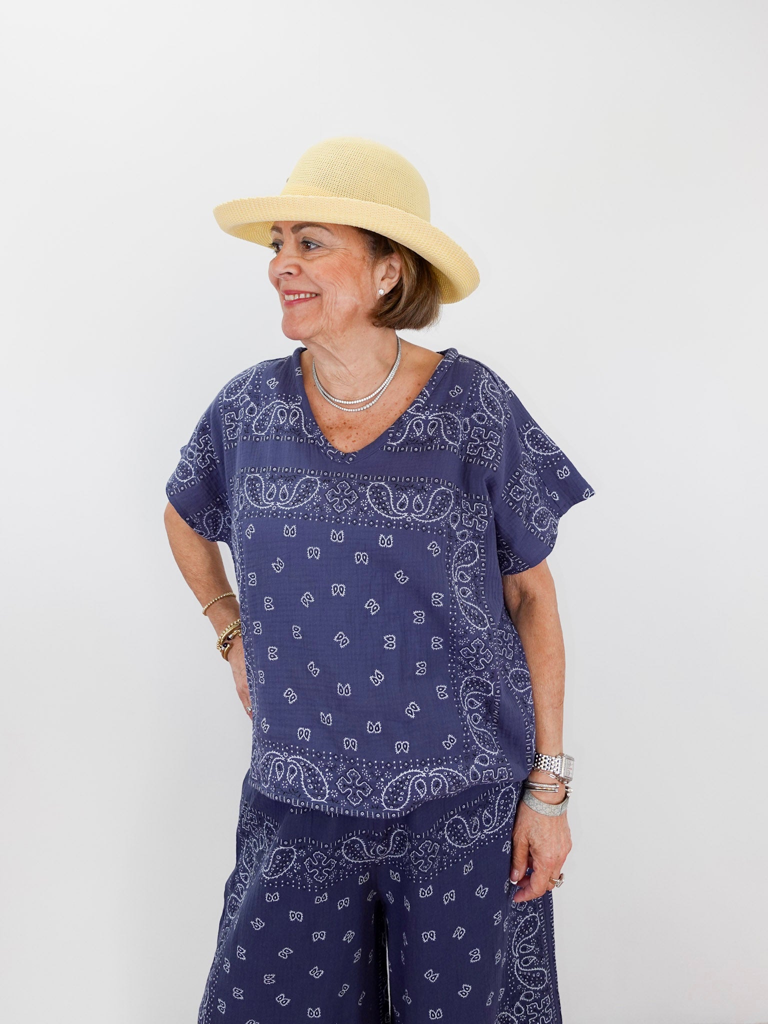 Woman wearing a blue paisley outfit with a beige hat on a white background