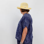 Person wearing a blue paisley patterned outfit and yellow hat against a white background