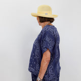 Person wearing a blue paisley patterned outfit and yellow hat against a white background