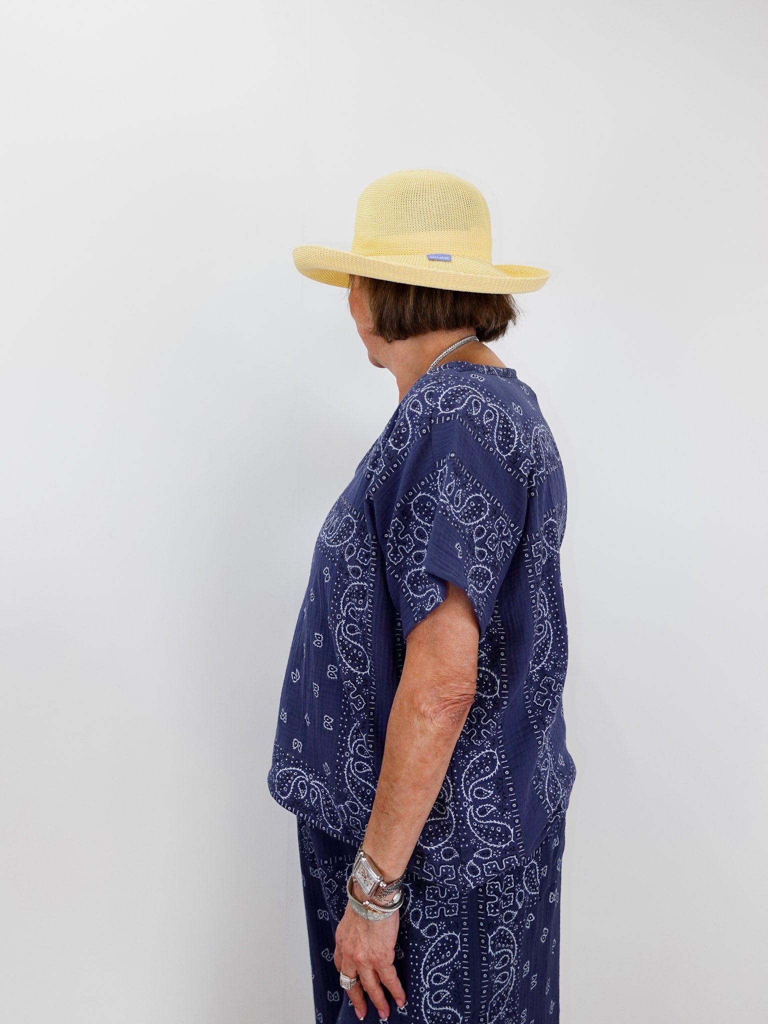 Person wearing a blue paisley patterned outfit and yellow hat against a white background