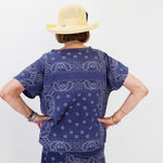 Person wearing a navy blue bandana print outfit with a beige hat on a white background
