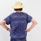 Person wearing a navy blue bandana print outfit with a beige hat on a white background
