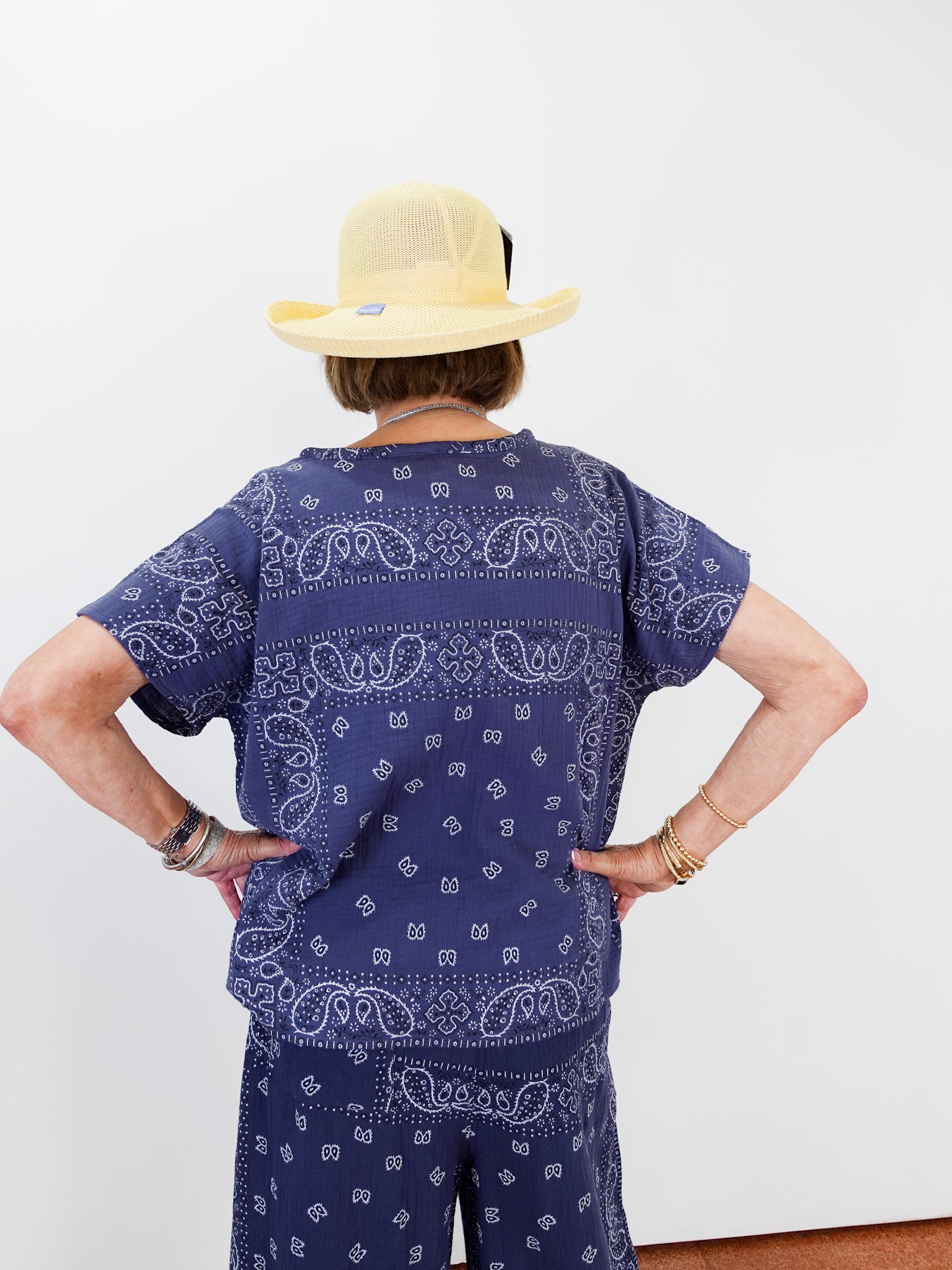 Person wearing a navy blue bandana print outfit with a beige hat on a white background