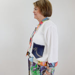 Person wearing a colorful outfit with a white shirt and patterned pants against a plain background