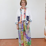 Woman wearing a colorful outfit with a patterned scarf and pants against a white wall.