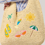 Woven bag with summer-themed embroidery held by a person wearing a striped shirt.
