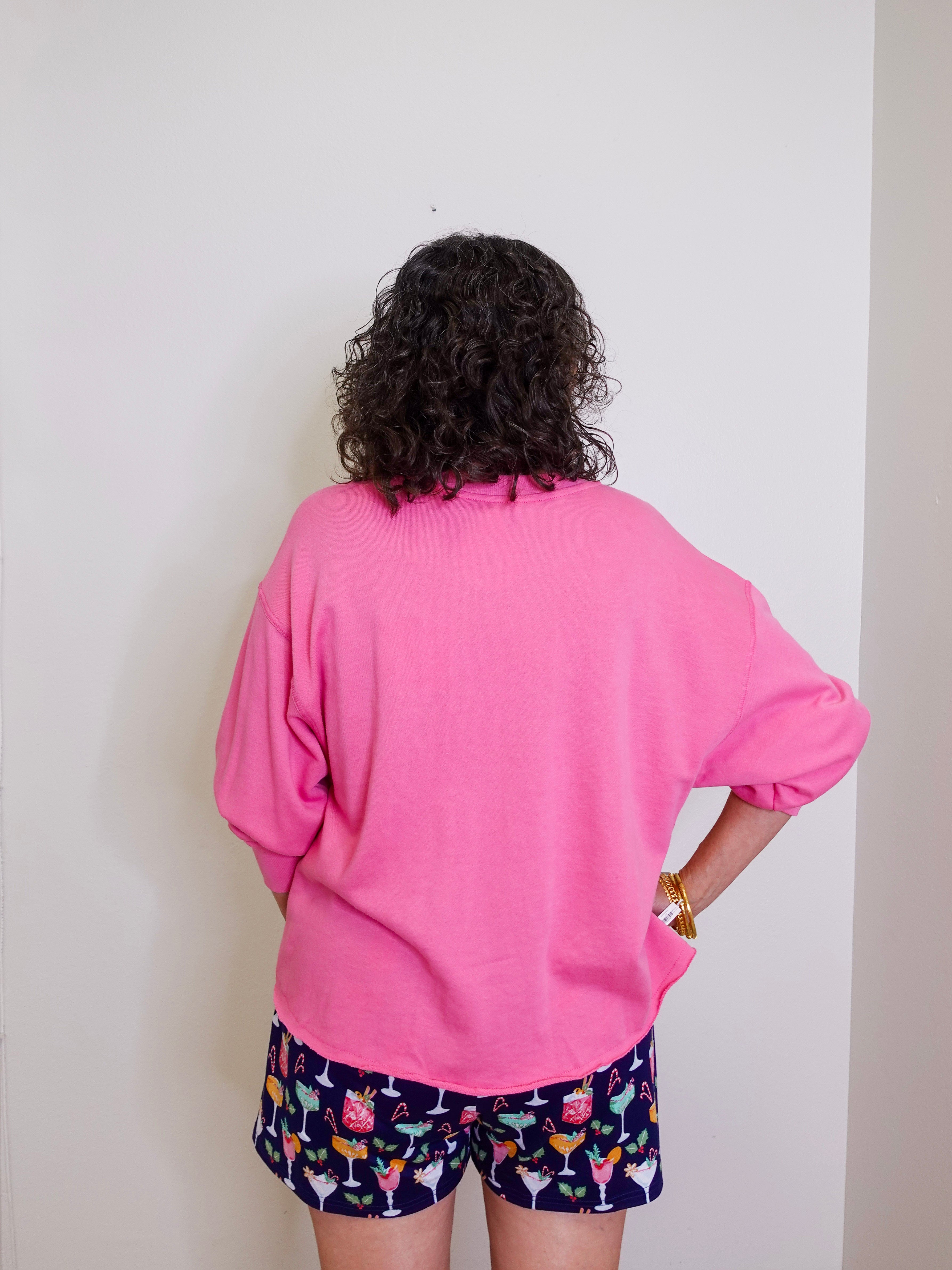 Person wearing a pink sweatshirt and patterned shorts against a plain background