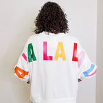 Person wearing a white sweatshirt with colorful letters on the back against a plain background
