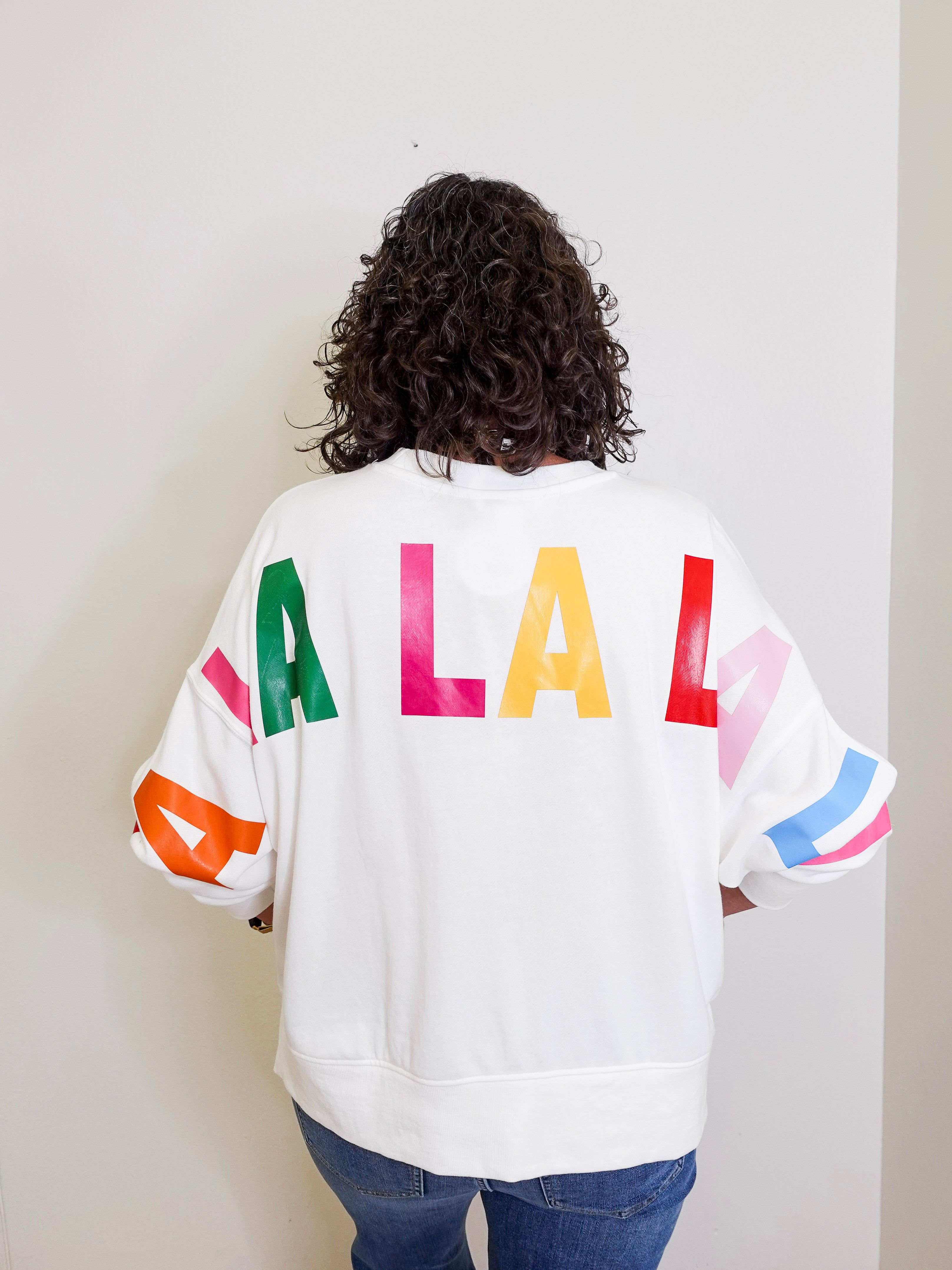 Person wearing a white sweatshirt with colorful letters on the back against a plain background