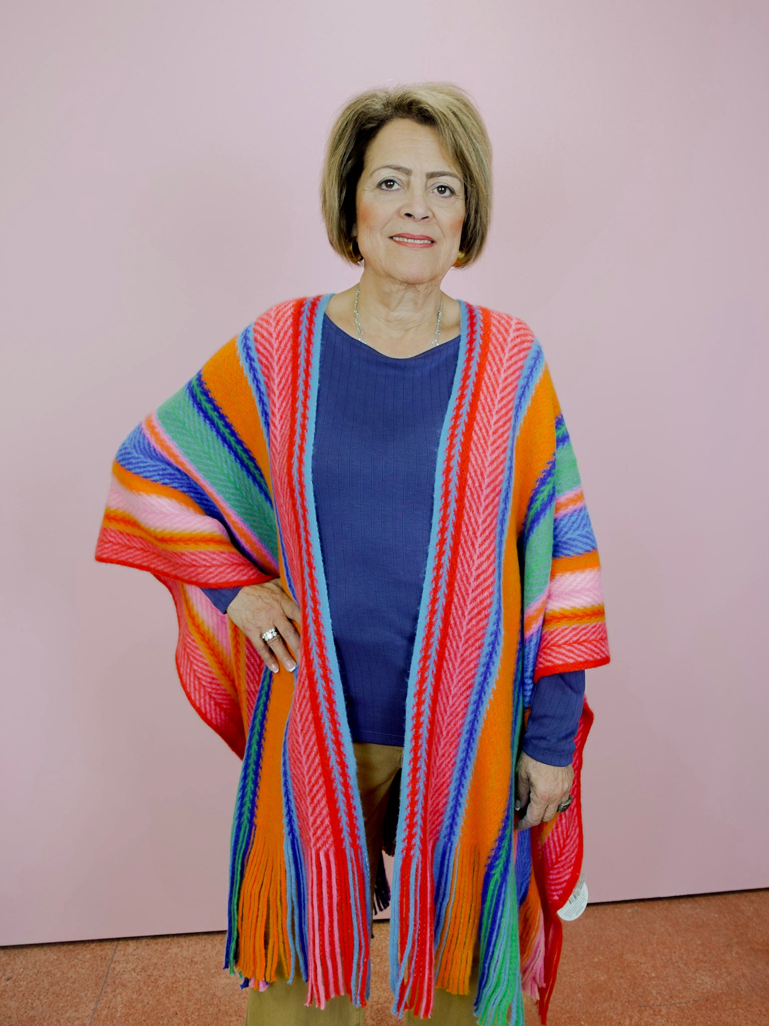 Woman wearing a colorful striped cardigan against a pink background