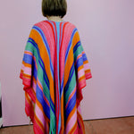 Person wearing a colorful striped poncho against a plain background