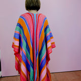 Person wearing a colorful striped poncho against a plain background