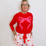 Person wearing a red sweater with a pink bow and white shorts with red patterns against a white background