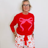 Person wearing a red sweater with a pink bow and white shorts with red patterns against a white background