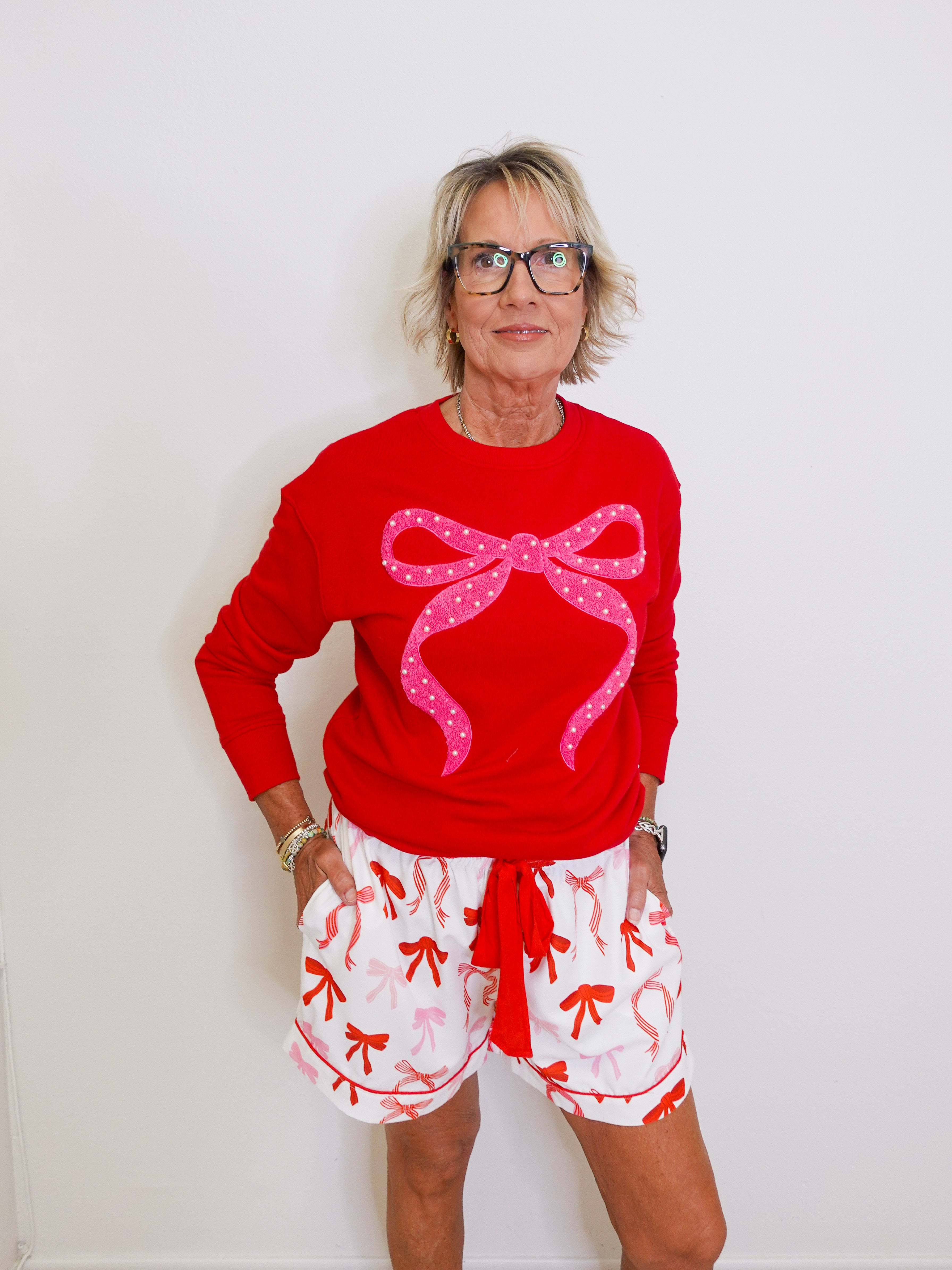 Person wearing a red sweater with a pink bow and white shorts with red patterns against a white background