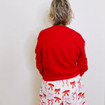 Person wearing a red sweatshirt and white shorts with red bows against a white wall