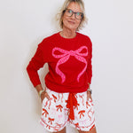 Person wearing a red sweater with a pink bow design and white shorts with red patterns on a white background