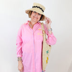 Woman wearing a pink shirt, blue jeans, and a straw hat with a palm tree design.