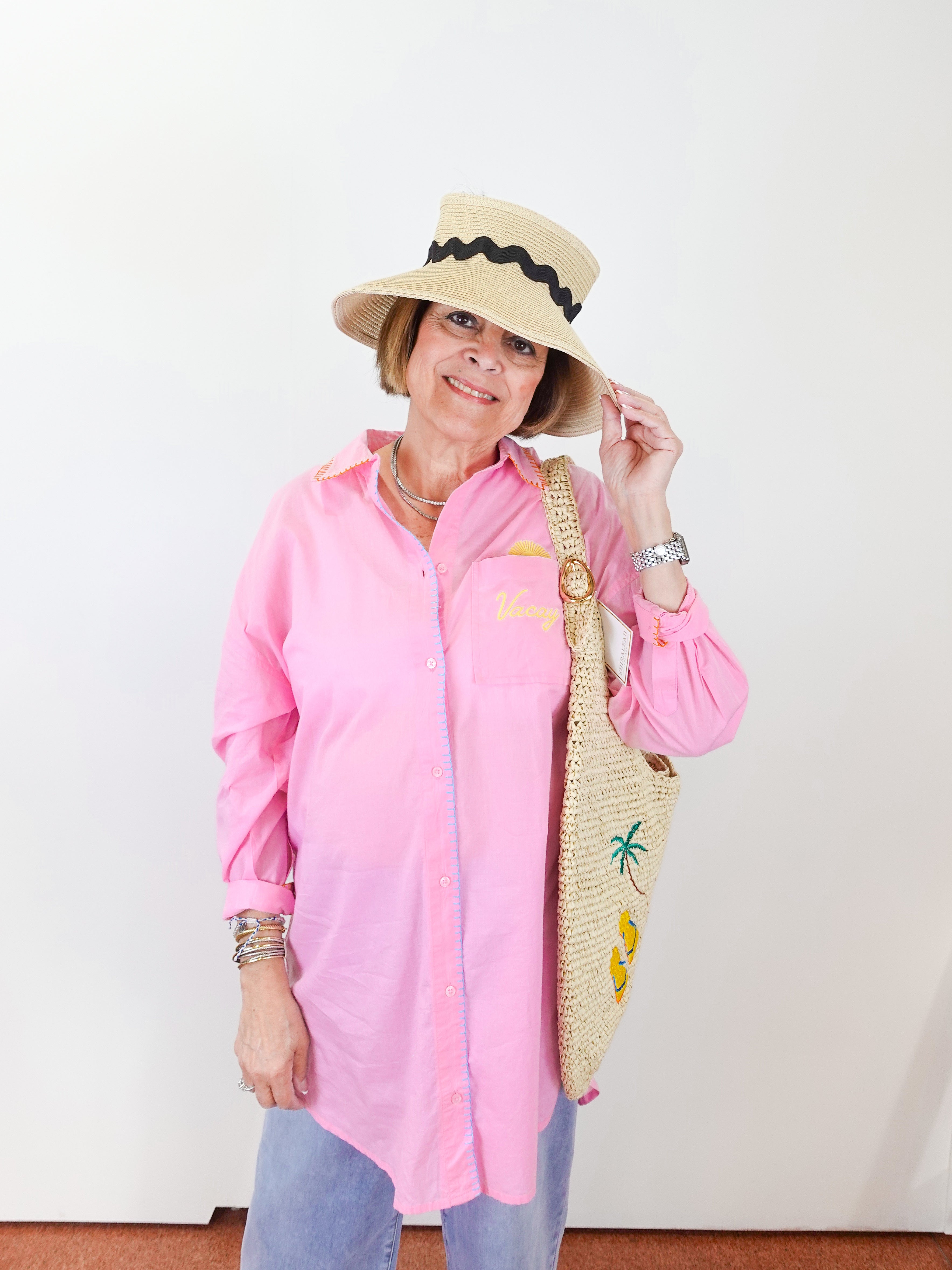 Woman wearing a pink shirt, blue jeans, and a straw hat with a palm tree design.
