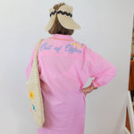 Person wearing a pink shirt with 'Out of Office' text, standing against a white wall.