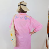 Person wearing a pink shirt with 'Out of Office' text, standing against a white wall.