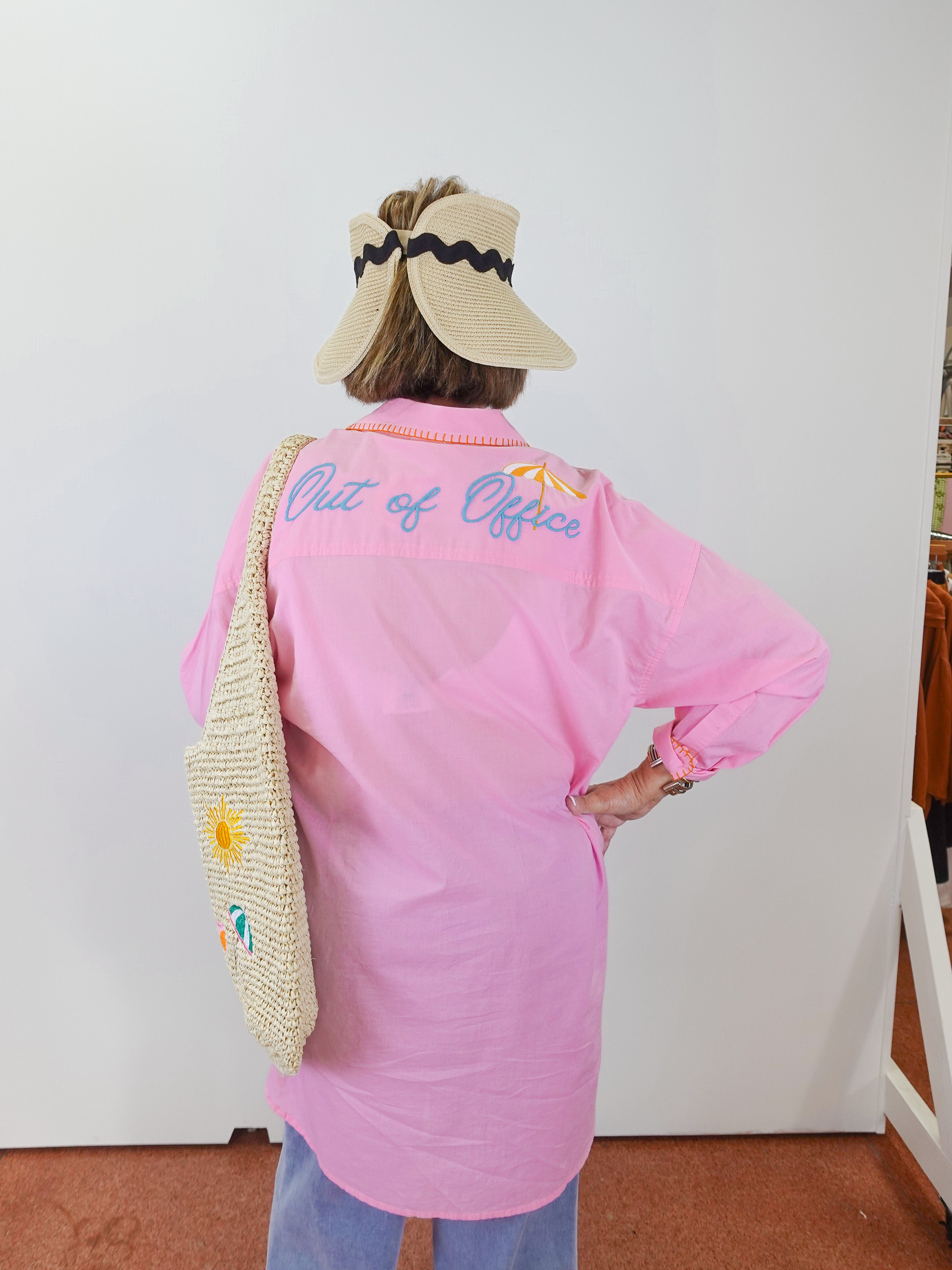 Person wearing a pink shirt with 'Out of Office' text, standing against a white wall.