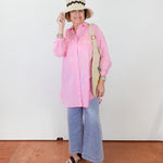 Person wearing a pink shirt, blue jeans, and a straw hat with a black band on a white background.
