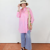 Person wearing a pink shirt, blue jeans, and a straw hat with a black band on a white background.