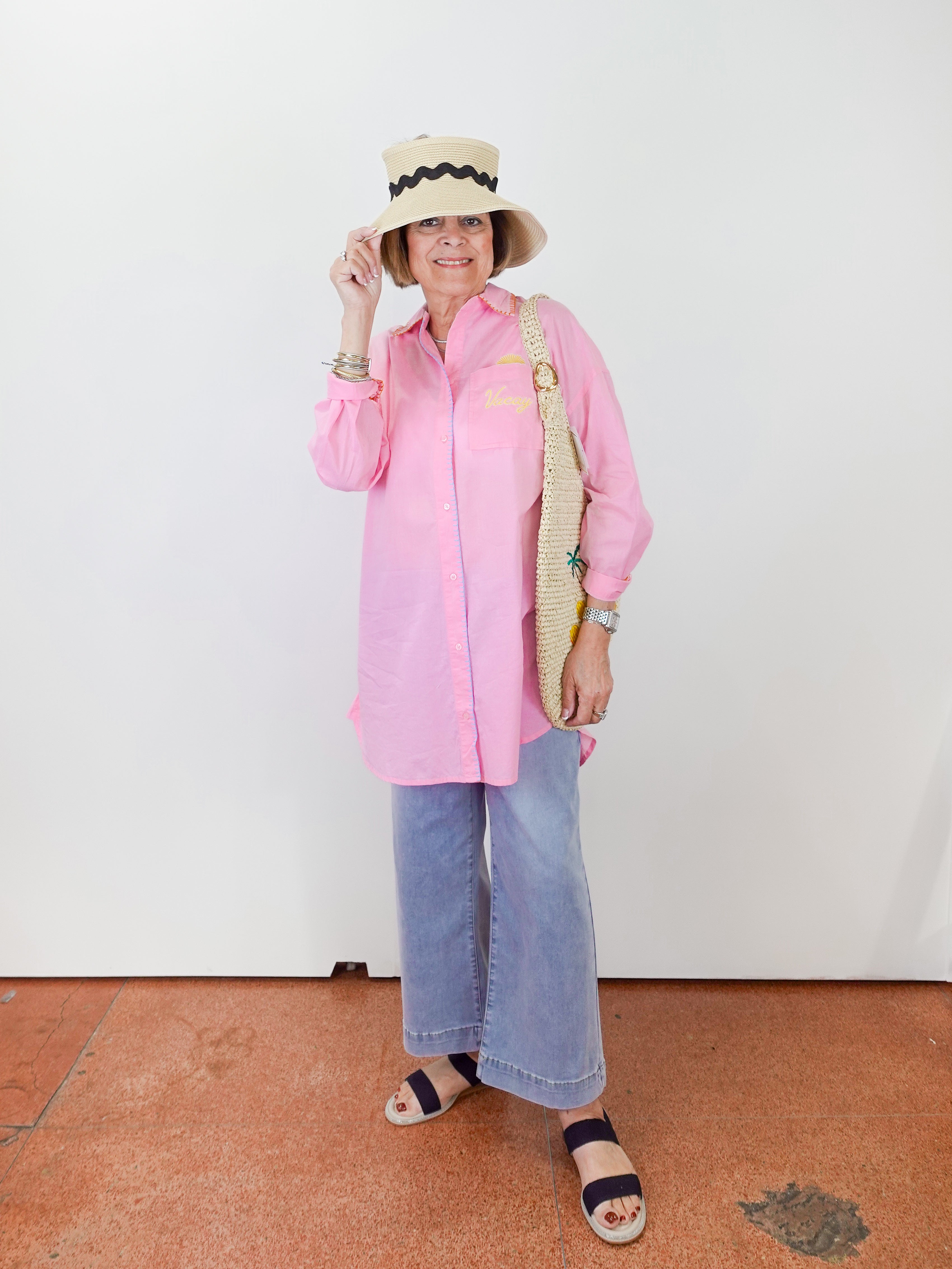 Person wearing a pink shirt, blue jeans, and a straw hat with a black band on a white background.