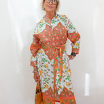 Woman wearing a colorful floral dress against a white wall.