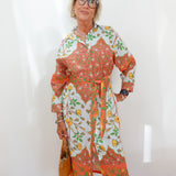 Woman wearing a colorful floral dress against a white wall.