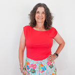 Woman wearing a red top and floral skirt against a white background